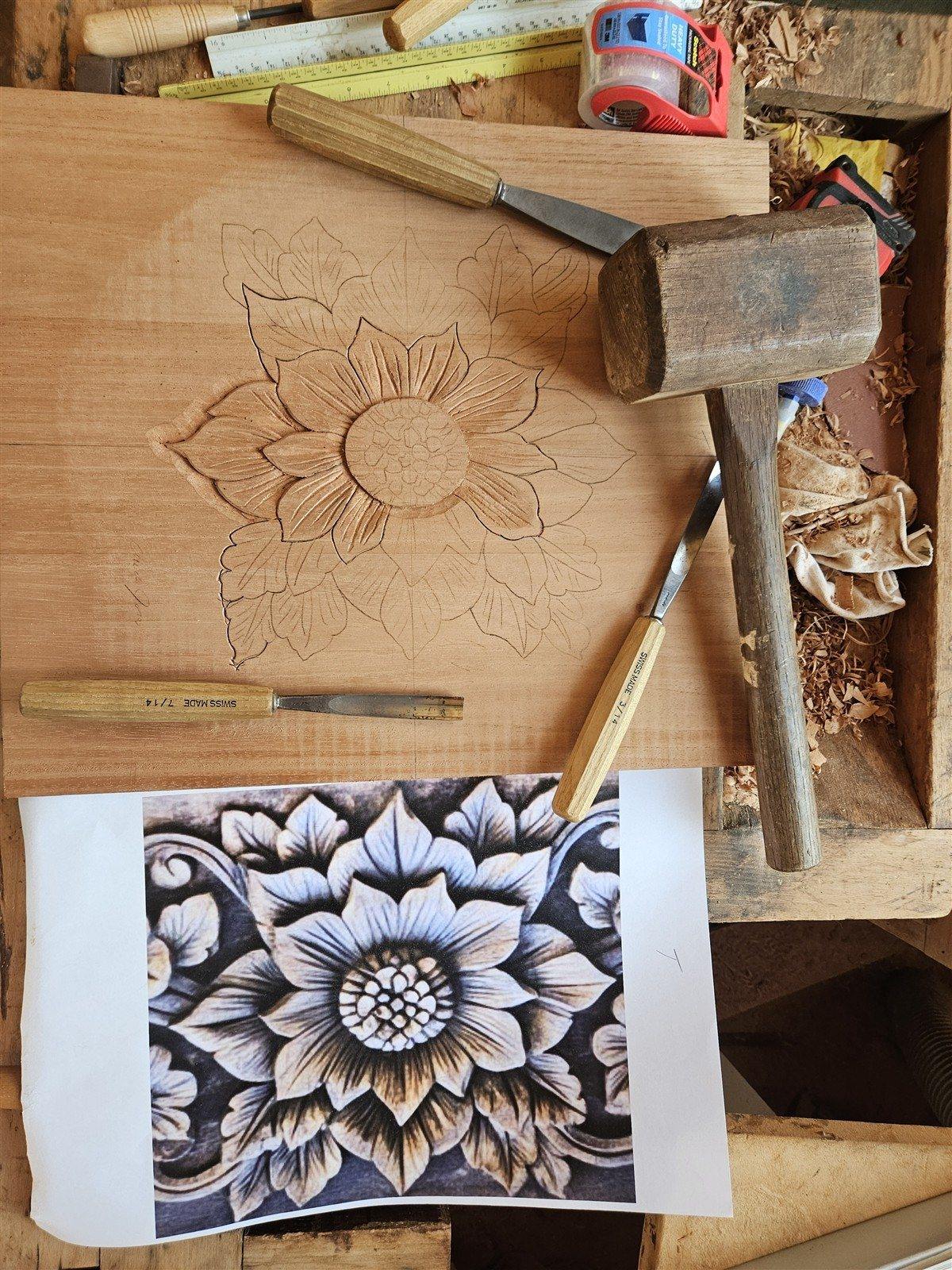 Partly carved flower on a workbench with chisels, mallet, and reference drawing